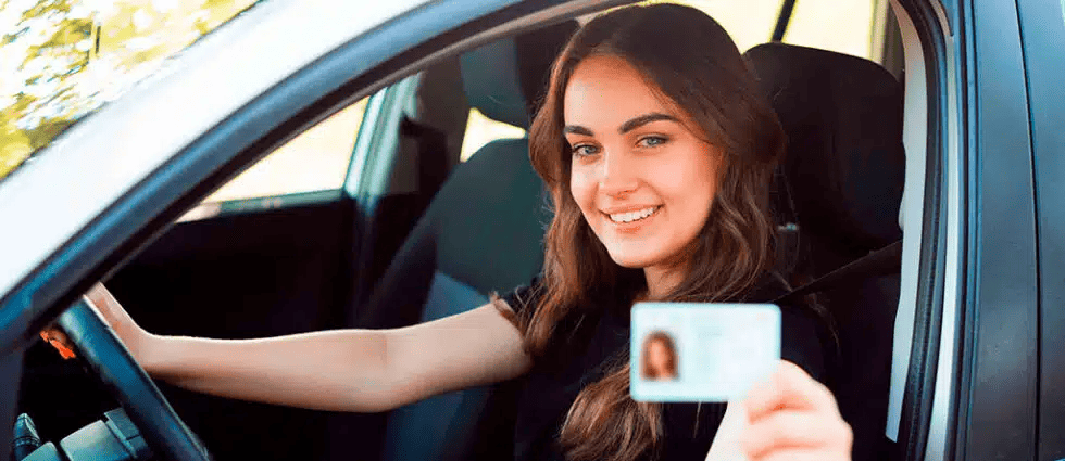 mujer joven sosteniendo licencia de conducir en vehiculo con sonrisa